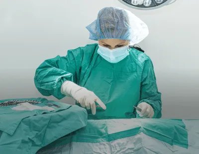 Veterinary surgeon in green scrubs and mask performing a surgical procedure in a modern operating room, emphasizing pet surgery services at Pilina Vet.