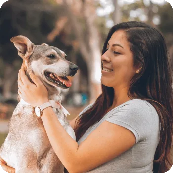 Woman joyfully holding and interacting with a dog, showcasing a bond of care and affection, reflecting the compassionate veterinary services highlighted in client testimonials for Pilina Vet.
