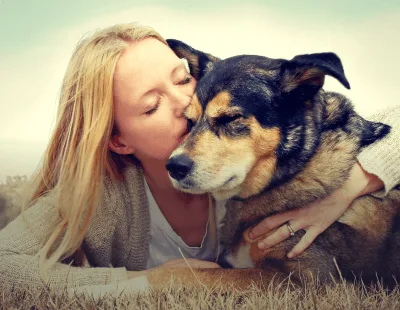 Woman kissing her dog in a peaceful outdoor setting, emphasizing love and connection, relevant to compassionate pet euthanasia services at Pilina Vet.