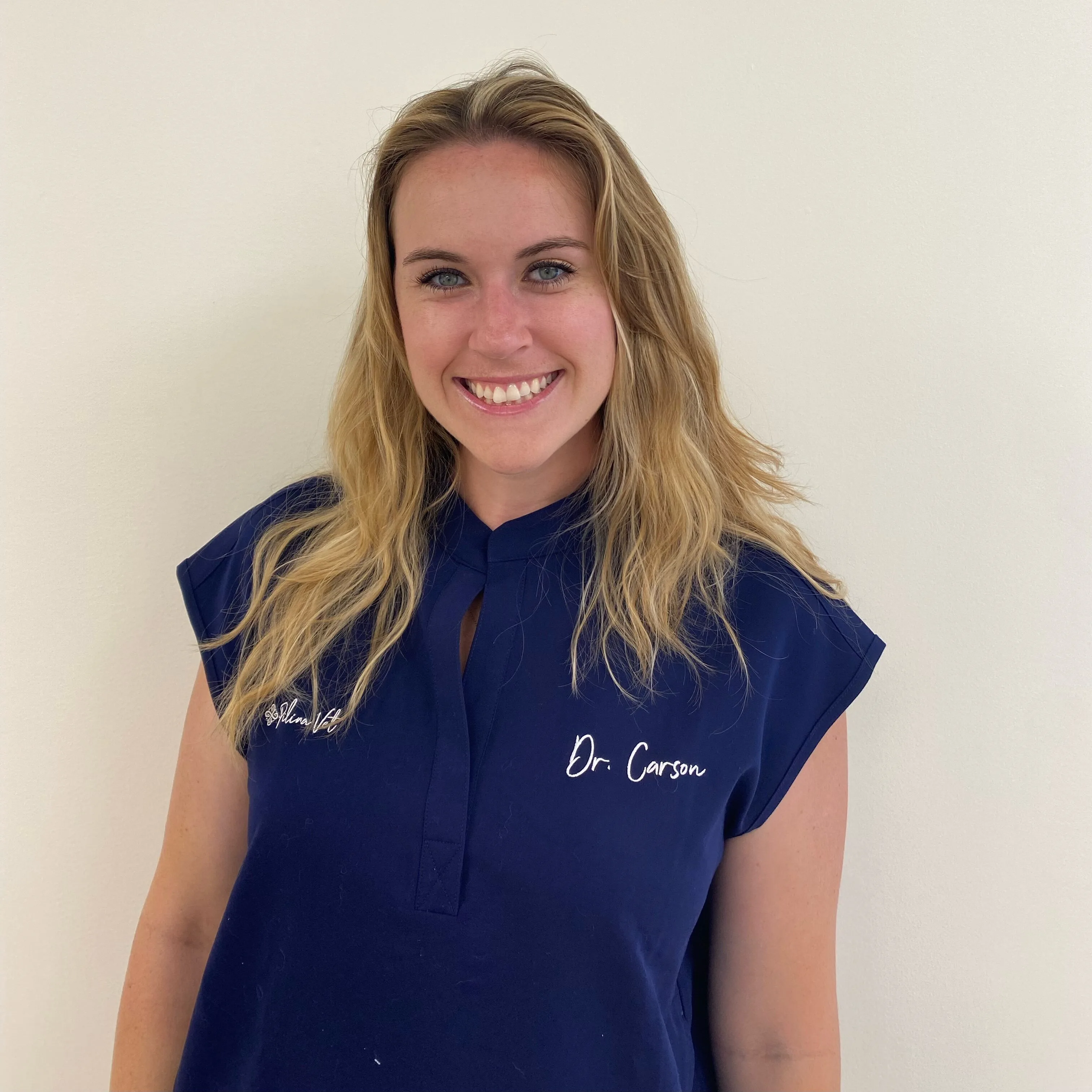 Dr. Carson, associate veterinarian at Pilina Vet, smiling in a navy blue veterinary shirt with her name embroidered, against a plain background.