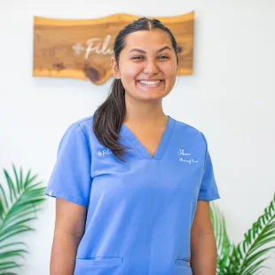 Veterinary Nurse Joleen Pregil in blue scrubs, smiling in front of Pilina Vet logo, showcasing her role in providing quality pet care.
